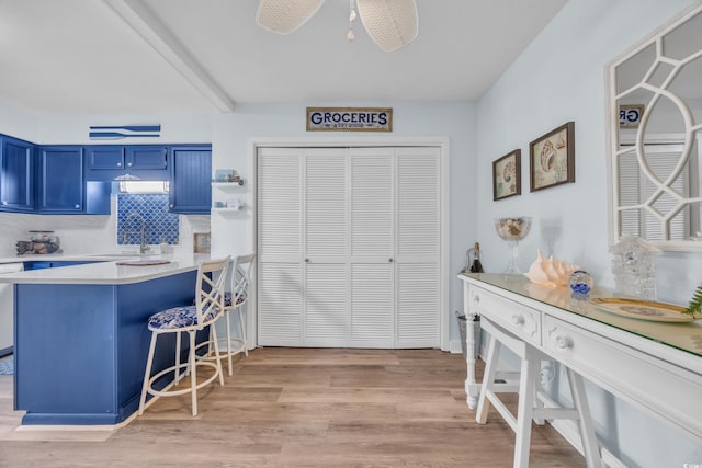 kitchen featuring light wood finished floors, blue cabinetry, light countertops, a sink, and a kitchen breakfast bar