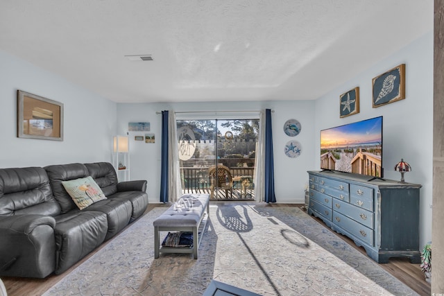 living room featuring visible vents, a textured ceiling, baseboards, and wood finished floors