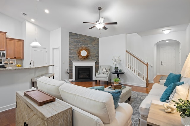 living room featuring arched walkways, dark wood-type flooring, a fireplace with flush hearth, visible vents, and stairs