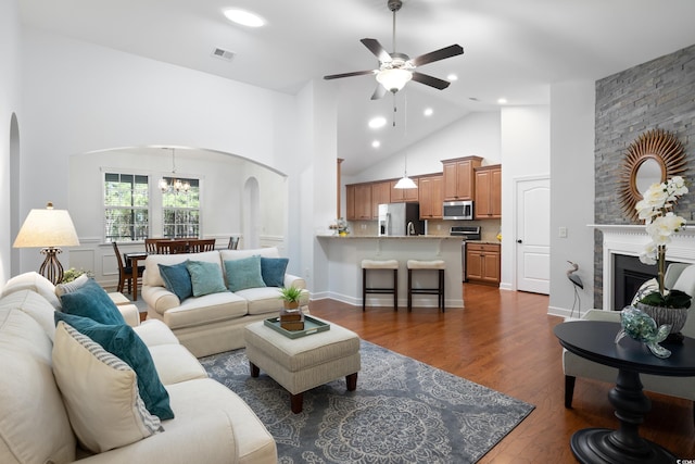 living room featuring arched walkways, dark wood-style flooring, visible vents, a large fireplace, and high vaulted ceiling