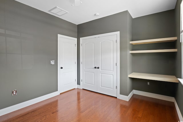 unfurnished bedroom featuring a closet, visible vents, baseboards, and wood finished floors