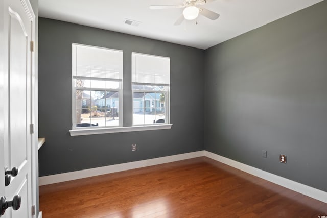 empty room featuring ceiling fan, visible vents, baseboards, and wood finished floors