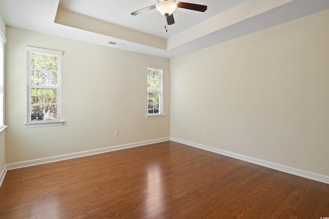 empty room with dark wood-style floors, visible vents, a tray ceiling, and a wealth of natural light