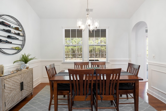 dining space with arched walkways, visible vents, a decorative wall, dark wood-type flooring, and a chandelier