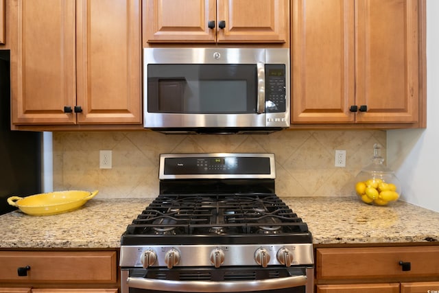 kitchen with appliances with stainless steel finishes, light stone counters, and decorative backsplash