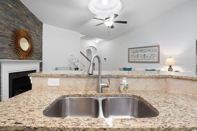 kitchen featuring light stone countertops, a fireplace, vaulted ceiling, and a sink