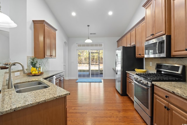 kitchen featuring a sink, appliances with stainless steel finishes, light wood-type flooring, light stone countertops, and decorative light fixtures