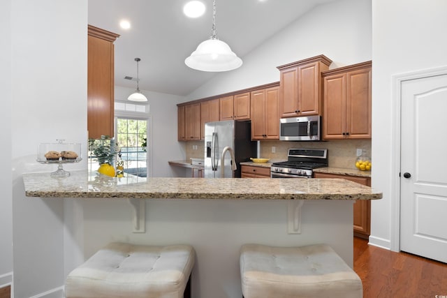 kitchen with vaulted ceiling, a peninsula, appliances with stainless steel finishes, and a breakfast bar