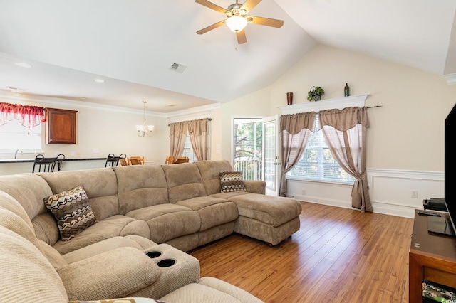 living area with visible vents, lofted ceiling, crown molding, light wood-type flooring, and ceiling fan with notable chandelier