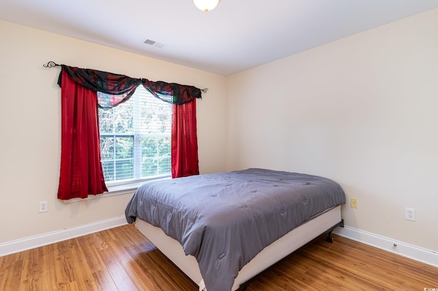 bedroom with baseboards, visible vents, and wood finished floors