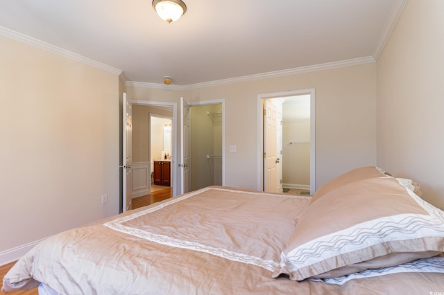 bedroom featuring baseboards, wood finished floors, a walk in closet, and crown molding