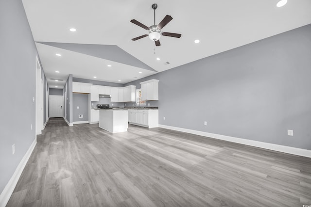 unfurnished living room featuring vaulted ceiling, ceiling fan, light wood-style floors, and baseboards