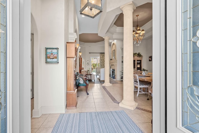 foyer entrance with a chandelier, light tile patterned flooring, decorative columns, and crown molding