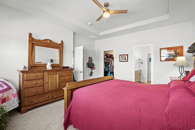 bedroom featuring a tray ceiling, a walk in closet, a closet, light carpet, and ensuite bath