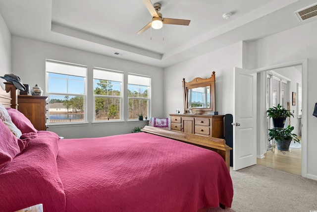 carpeted bedroom with baseboards, visible vents, a raised ceiling, and a ceiling fan