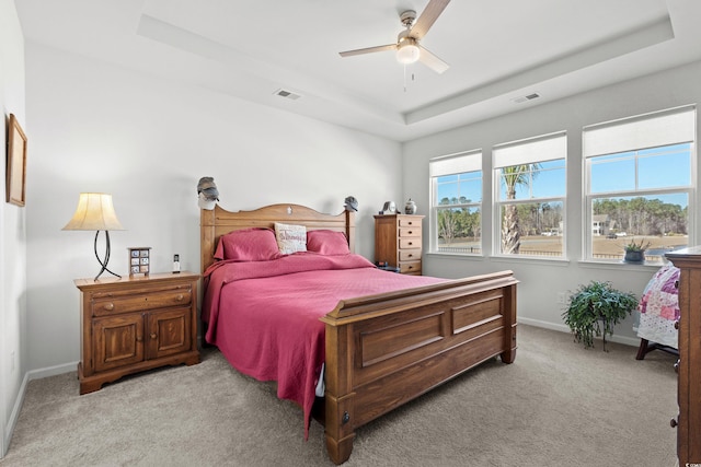 bedroom with light carpet, visible vents, a tray ceiling, and baseboards