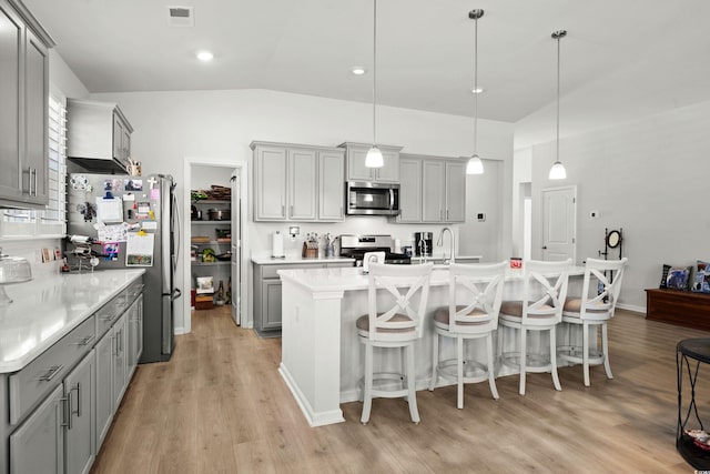 kitchen featuring light wood-style flooring, gray cabinetry, stainless steel appliances, visible vents, and a kitchen breakfast bar