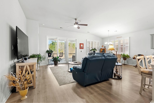 living area featuring ceiling fan with notable chandelier, visible vents, baseboards, vaulted ceiling, and light wood-style floors