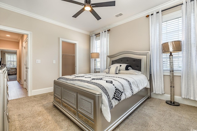 bedroom with light carpet, visible vents, baseboards, ornamental molding, and a walk in closet