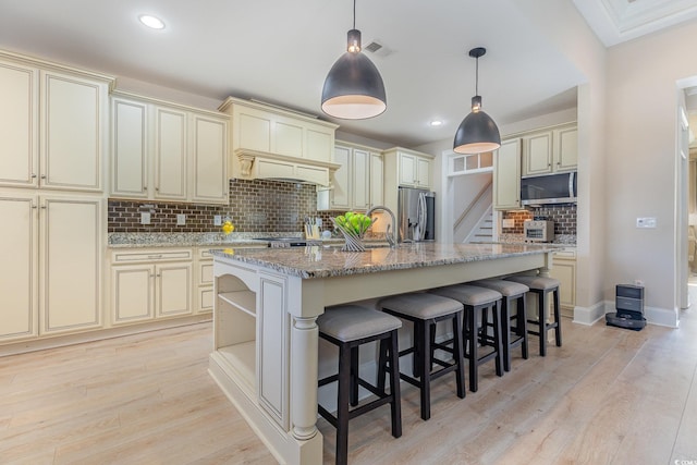 kitchen featuring light wood finished floors, cream cabinets, appliances with stainless steel finishes, and light stone counters