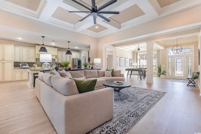 living room with ceiling fan with notable chandelier, beam ceiling, light wood-type flooring, and decorative columns