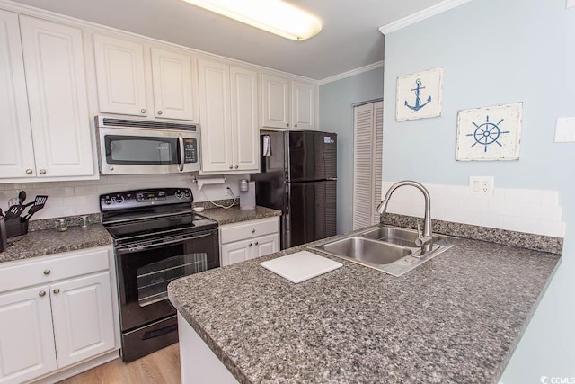 kitchen featuring dark countertops, ornamental molding, a peninsula, black appliances, and a sink