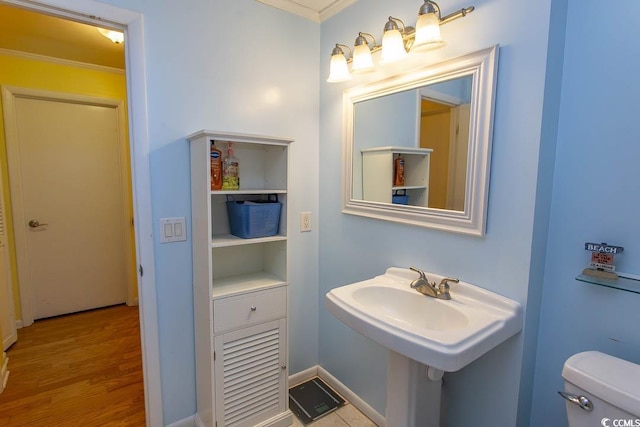 half bathroom featuring toilet, a sink, ornamental molding, and wood finished floors