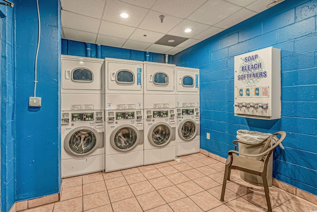 community laundry room featuring stacked washer / dryer, tile patterned flooring, washer and clothes dryer, and concrete block wall