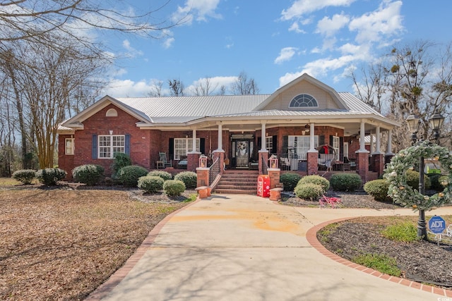 view of front of home featuring covered porch, metal roof, and brick siding