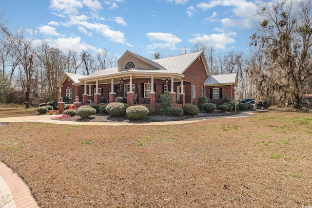 view of front of property with metal roof, a porch, a front yard, and brick siding