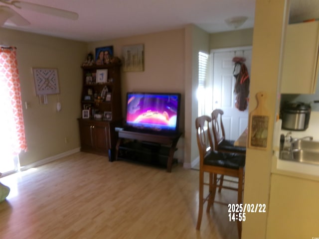 living room featuring light wood finished floors, a ceiling fan, and baseboards