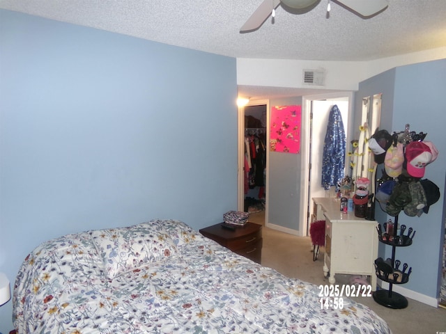 carpeted bedroom with baseboards, visible vents, a ceiling fan, a walk in closet, and a textured ceiling