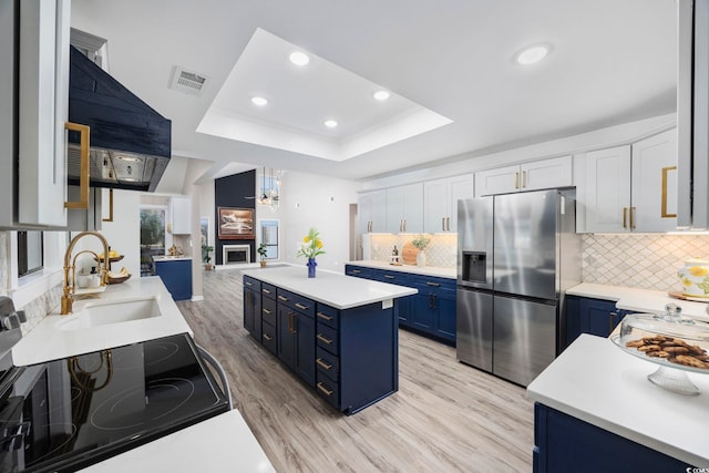 kitchen featuring blue cabinetry, a raised ceiling, visible vents, a sink, and stainless steel fridge