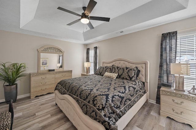 bedroom featuring a tray ceiling, light wood-style flooring, baseboards, and visible vents