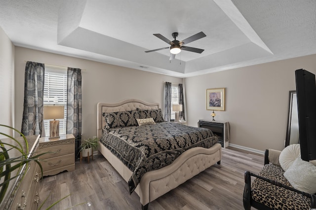 bedroom with a textured ceiling, a raised ceiling, baseboards, and wood finished floors