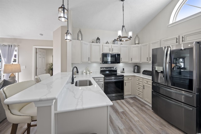 kitchen with lofted ceiling, light stone counters, appliances with stainless steel finishes, a peninsula, and a sink