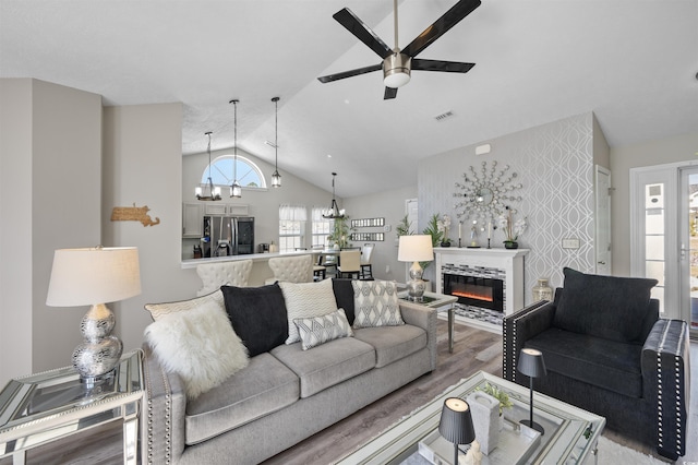 living room with visible vents, an accent wall, vaulted ceiling, light wood-style floors, and a glass covered fireplace