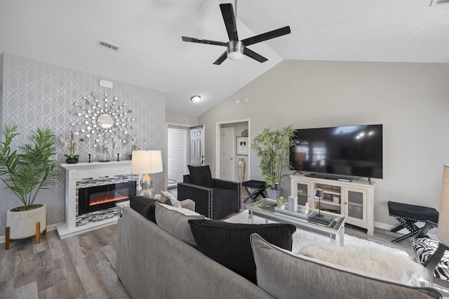 living area with an accent wall, wood finished floors, visible vents, wallpapered walls, and a glass covered fireplace