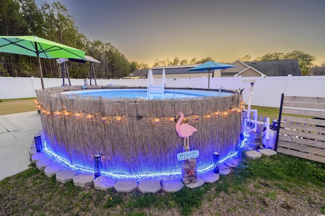 pool at dusk with a fenced backyard and a fenced in pool