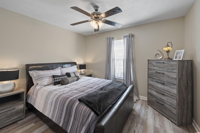 bedroom featuring ceiling fan, a textured ceiling, baseboards, and light wood-style floors