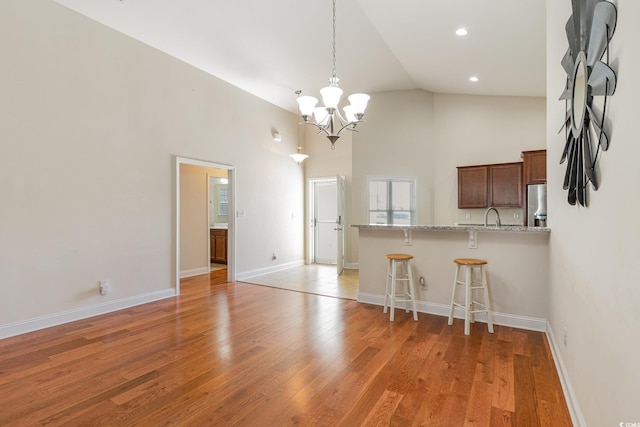 kitchen with a breakfast bar area, high vaulted ceiling, light wood-type flooring, stainless steel fridge, and a peninsula