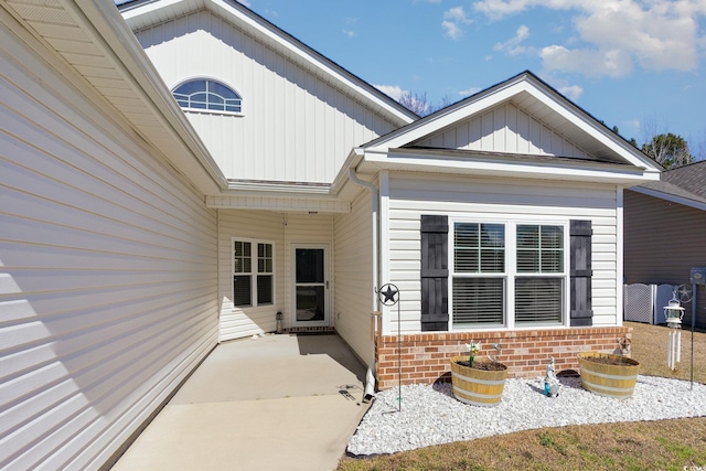 view of exterior entry featuring a patio, brick siding, and board and batten siding