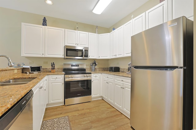 kitchen featuring light wood finished floors, appliances with stainless steel finishes, light stone counters, white cabinetry, and a sink