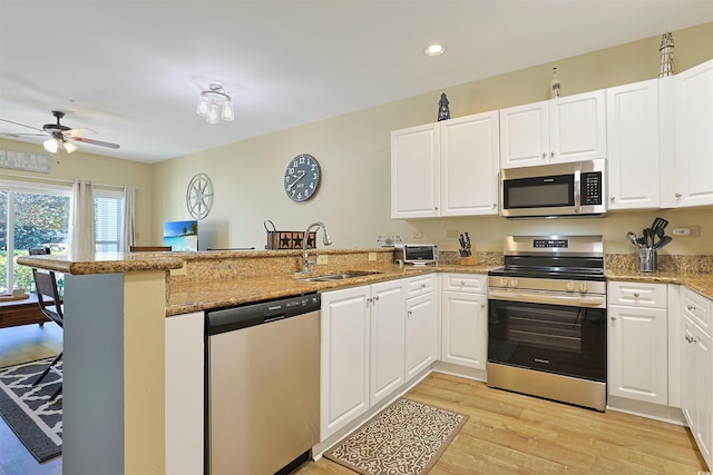 kitchen featuring white cabinets, light wood-style flooring, appliances with stainless steel finishes, a peninsula, and a sink