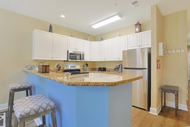 kitchen with light wood finished floors, visible vents, appliances with stainless steel finishes, a breakfast bar, and a peninsula