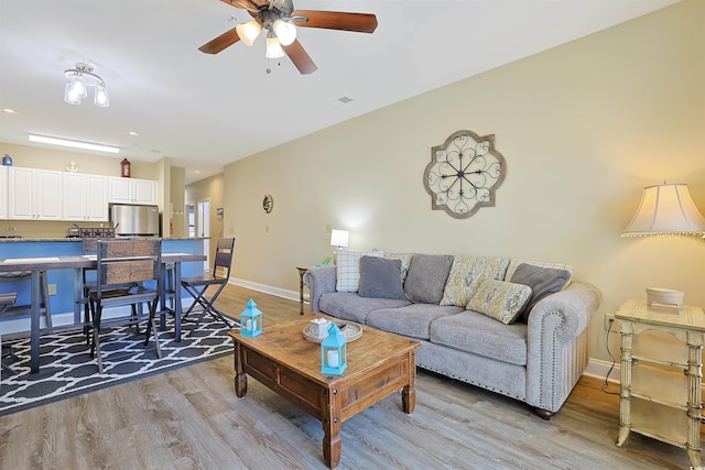 living room featuring a ceiling fan, light wood-type flooring, visible vents, and baseboards