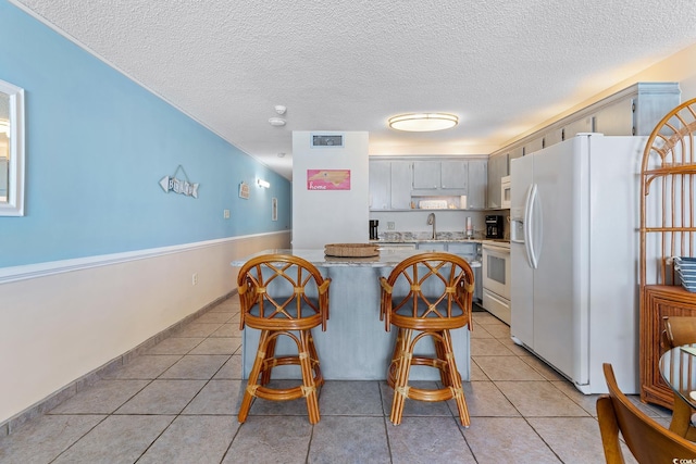 kitchen featuring light tile patterned floors, white appliances, visible vents, a kitchen bar, and a sink