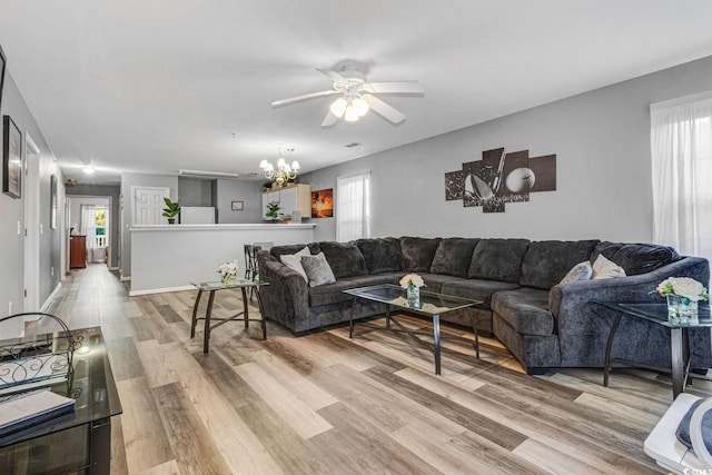 living room featuring baseboards, light wood finished floors, and ceiling fan with notable chandelier