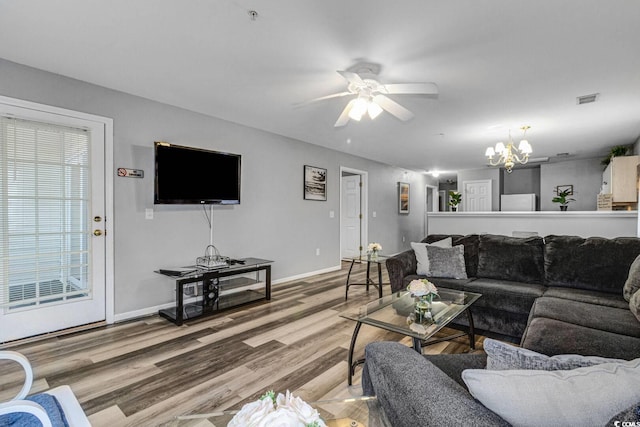 living room featuring light wood-type flooring, baseboards, visible vents, and ceiling fan with notable chandelier