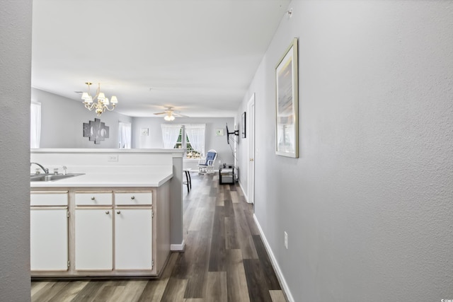 kitchen featuring dark wood-style flooring, light countertops, a sink, a peninsula, and baseboards